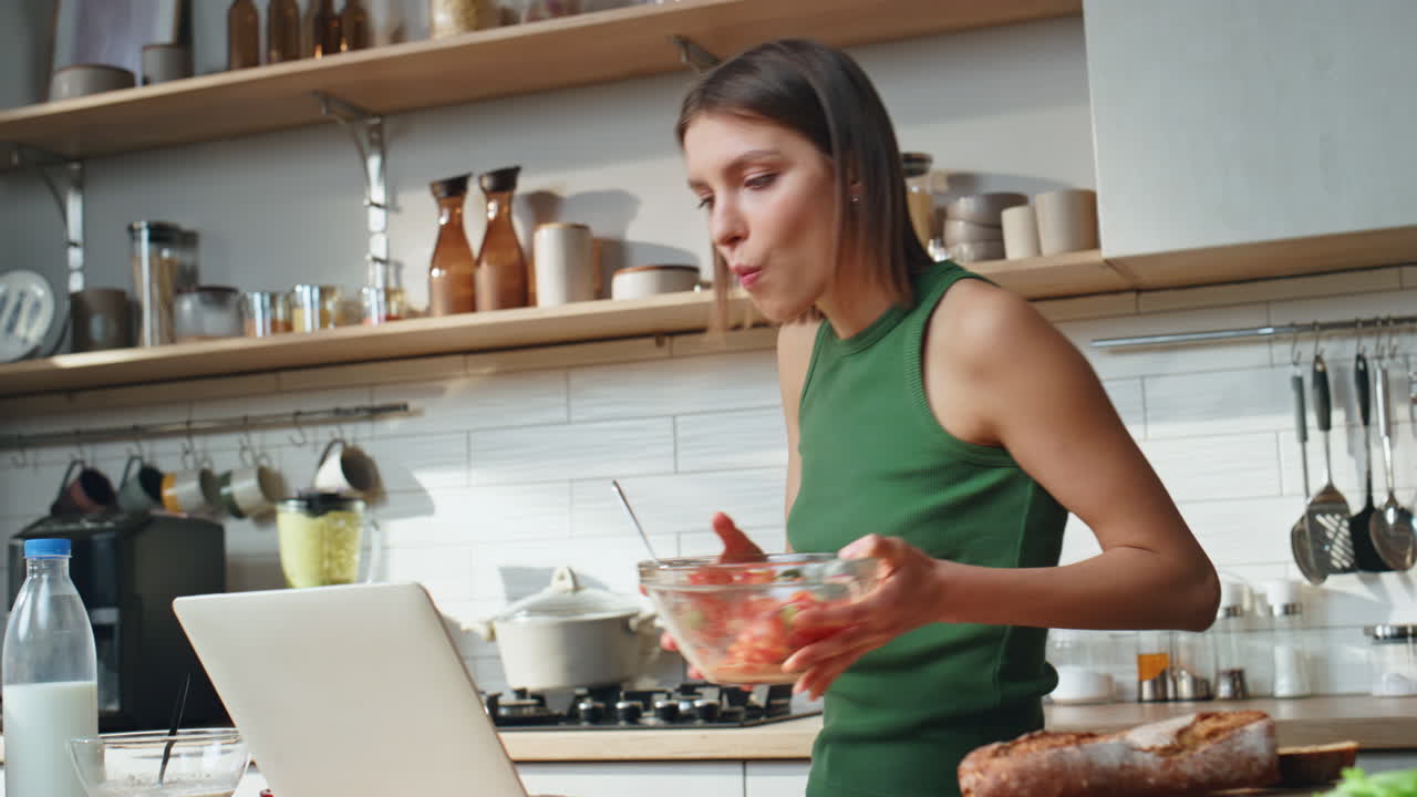 Woman Eating Salad While Working on Laptop in Kitchen