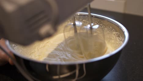 Electric-machine-mixing-delicious-whipped-cream-in-steel-bowl,-close-up-view