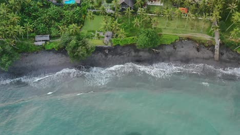 Arriba-Hacia-Abajo-De-La-Playa-Tropical-Jasri-Con-Olas-Turquesas-Del-Océano-Rompiendo-En-Arena-Negra-En-Bali,-Antena