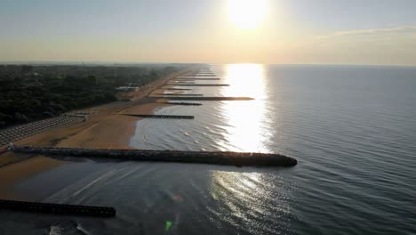 Aerial-flying-over-a-calm-Adriatic-sea-at-sunset-on-the-coast-of-Caorle,-a-town-of-Venice-in-Italy