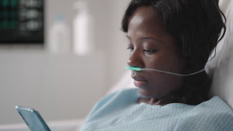 a young woman writes a message on her phone while lying in a hospital ward. an african girl is lying in a ward connected to ecg and oxygen devices in a mask and writes messages to relatives