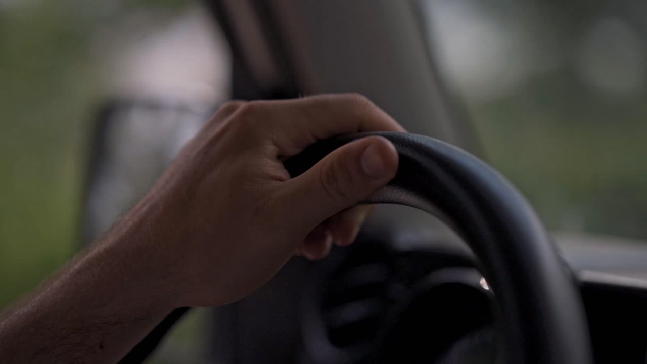 hand gripping a car's steering wheel, with the blurred, green landscape of Costa Rica visible through the window