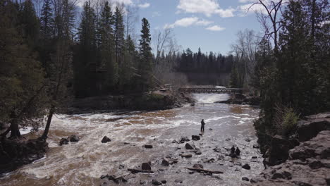 solitary fisherman fly fishing in forest river rapids