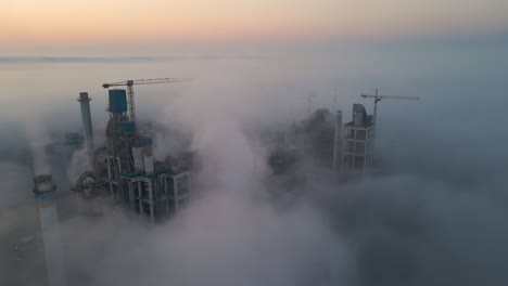 aerial view of cement factory with high concrete plant structure and tower crane at industrial production site on foggy morning. manufacture and global industry concept