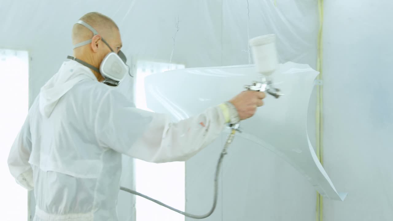 Mecánico pintando piezas de coche con pistola de pintura eléctrica 4k
