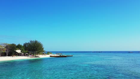 Aguas-Tranquilas-Y-Claras-De-Una-Laguna-Poco-Profunda-Que-Lava-La-Arena-Blanca-De-Una-Playa-Exótica,-Barcos-Anclados,-Bar-De-Playa-Frente-Al-Mar-En-Bali,-Indonesia