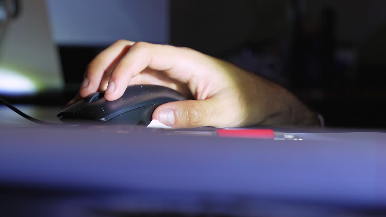 Close-up of a person's hand writing in a lined notebook with a red pen. The scene is dimly lit, suggesting a late-night study session or creative journaling in a home office