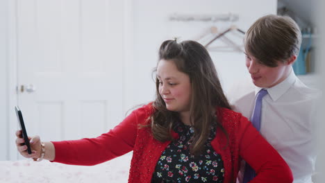 Loving-Young-Downs-Syndrome-Couple-Sitting-On-Bed-Using-Mobile-Phone-To-Take-Selfie-At-Home