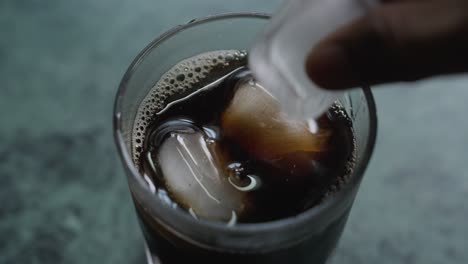 A closeup footage of a person's hand putting ice cubes in a glass of iced tea, with blurred background