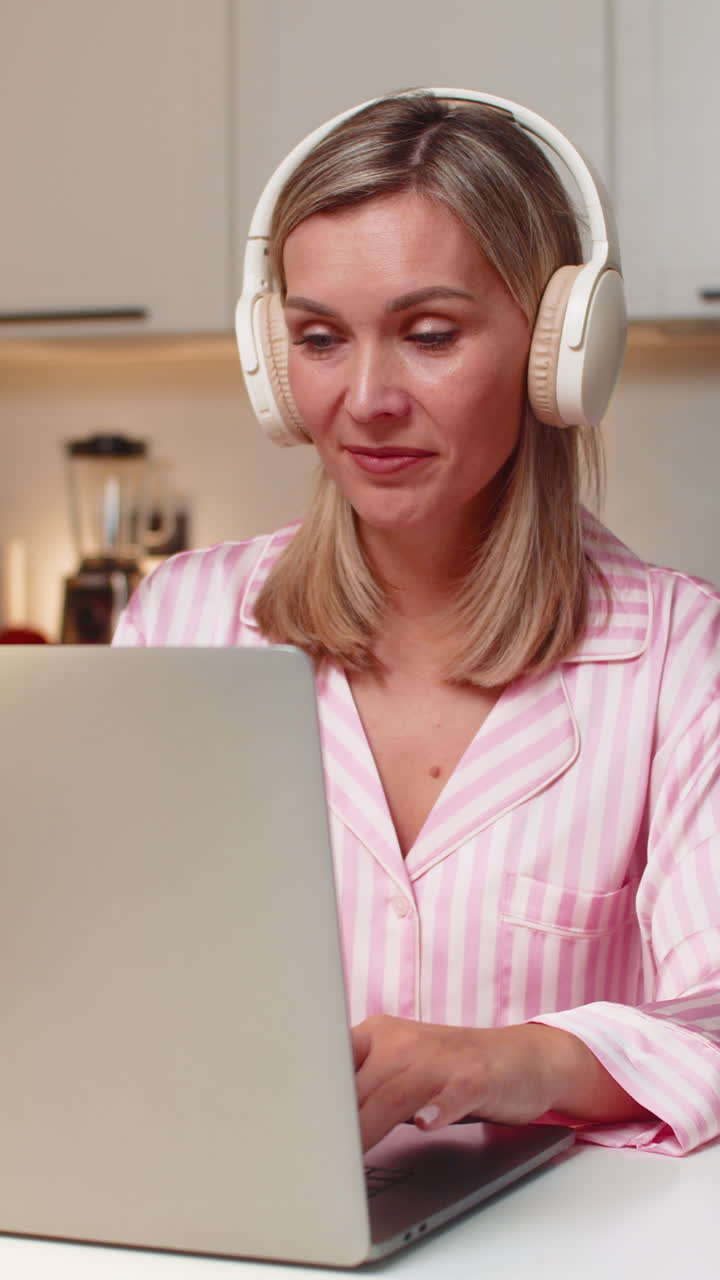 Adult woman freelancer edits layout on laptop in headphones smiles nods to music steady workflow