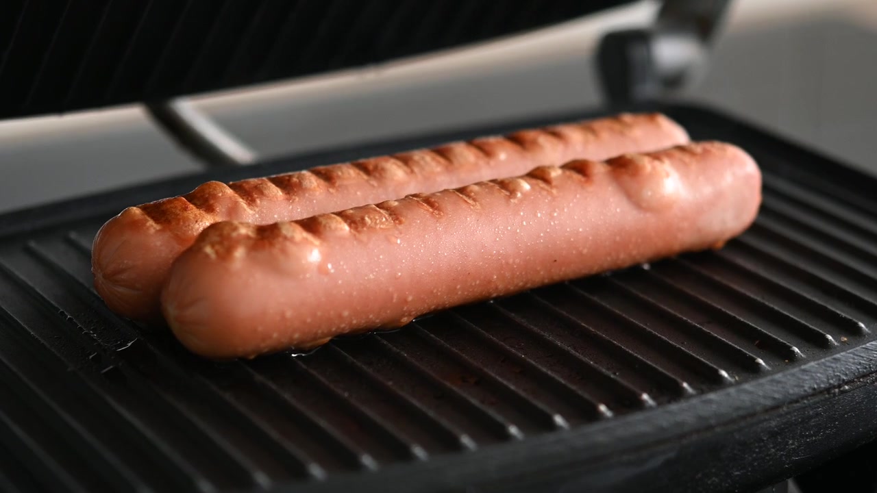 Hand som öppnar elgrill och avslöjar grillade korvar