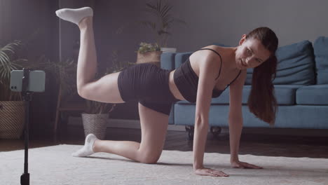 athletic female vlogger giving an online fitness class in front of her smartphone camera