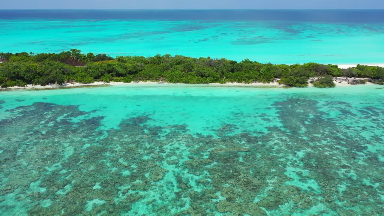 Calm turquoise lagoon with coral reefs surrounding tail o tropical island with white sandy beach and lush vegetation in Maldivian archipelago