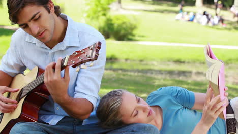el hombre practica la guitarra mientras la mujer lee su libro.