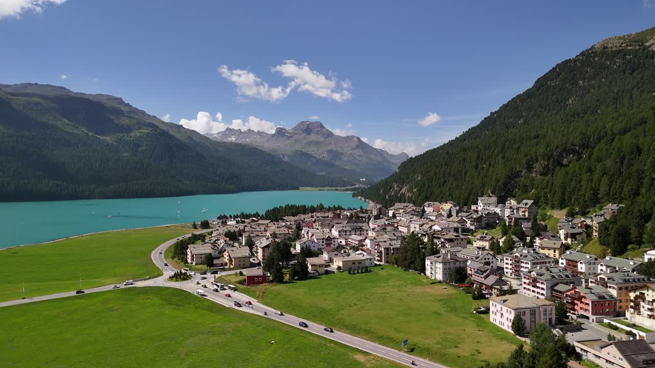 Aerial view of a road with traffic winding through the residential area near Lake Silvaplanersee in Silvaplana, Graubünden, Switzerland, capturing the blend of natural beauty and human activity.