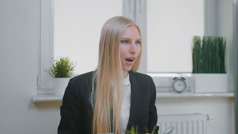 mujer celebrando el éxito en la oficina. elegante mujer rubia sentada en el lugar de trabajo sosteniendo en las manos un paquete de dinero mirando asombrado al monitor, y arrojando dinero en el aire y felizmente haciendo el gesto de sí.