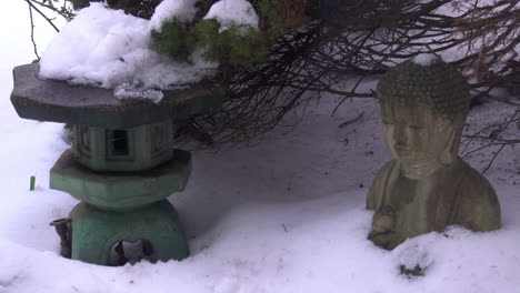 la nieve se derrite y gotea lentamente, apilada sobre una linterna japonesa y una estatua de buda
