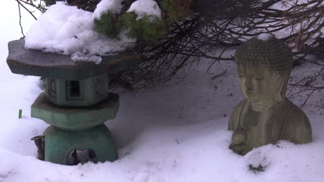 snow slowly melts and drips, piled atop a japanese lantern, and buddha statue