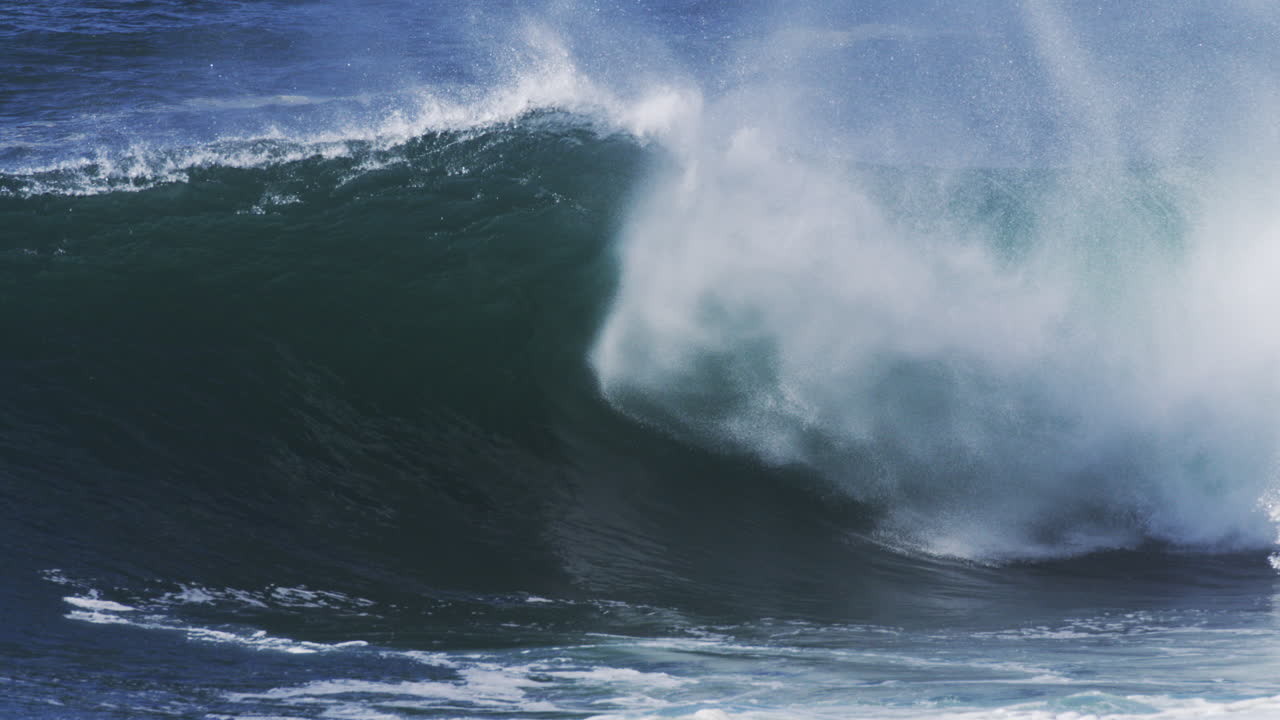 Dark barreling wave glows blue as fine mist lifts and spreads through the air