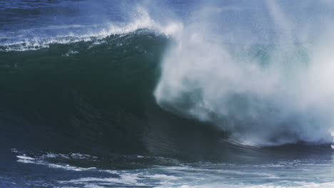 dark barreling wave glows blue as fine mist lifts and spreads through the air