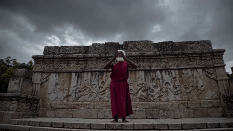 buddhist monk in traditional red robes standing on ancient stone steps with ornate carvings under a dramatic cloudy sky in polonnaruwa, sri lanka, radiating spirituality and heritage
