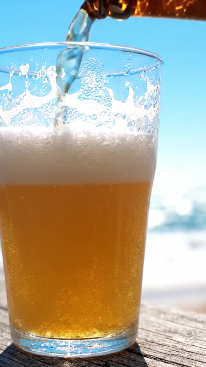 Birra fresca in un bicchiere sotto un cielo limpido, bollicine e schiuma creano la perfetta esperienza di una bevanda estiva in riva al mare