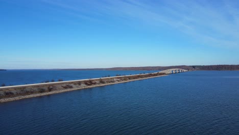 Elevación-Aérea-De-Un-Puente-Que-Se-Eleva-Sobre-Un-Lago-Azul-Con-Cielos-Azules