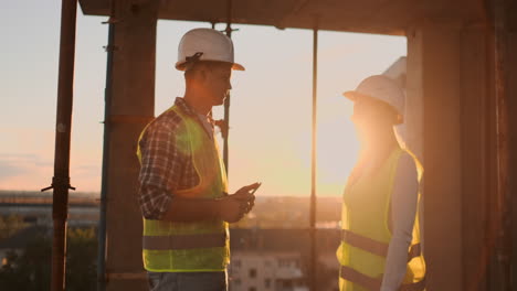 Guapos-Trabajadores-De-La-Construcción,-Hombres-Y-Mujeres,-Con-Cascos-Y-Chalecos-Protectores,-Se-Dan-La-Mano-Mientras-Trabajan-En-El-Centro-De-Oficinas