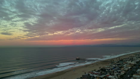 Panorámica-Aérea-De-La-Costa-De-La-Playa-Al-Atardecer-De-Manhattan-Beach,-California,-Horizonte-Americano-Con-Tonos-Rosados-Dorados,-Edificios-Frente-A-La-Costa