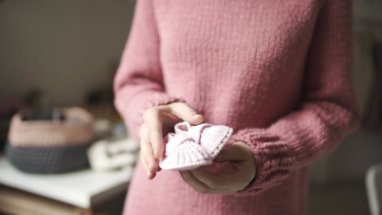 женские руки, показывающие вязаные детские ботинки. вязаные ботинки ручной работы для ребенка