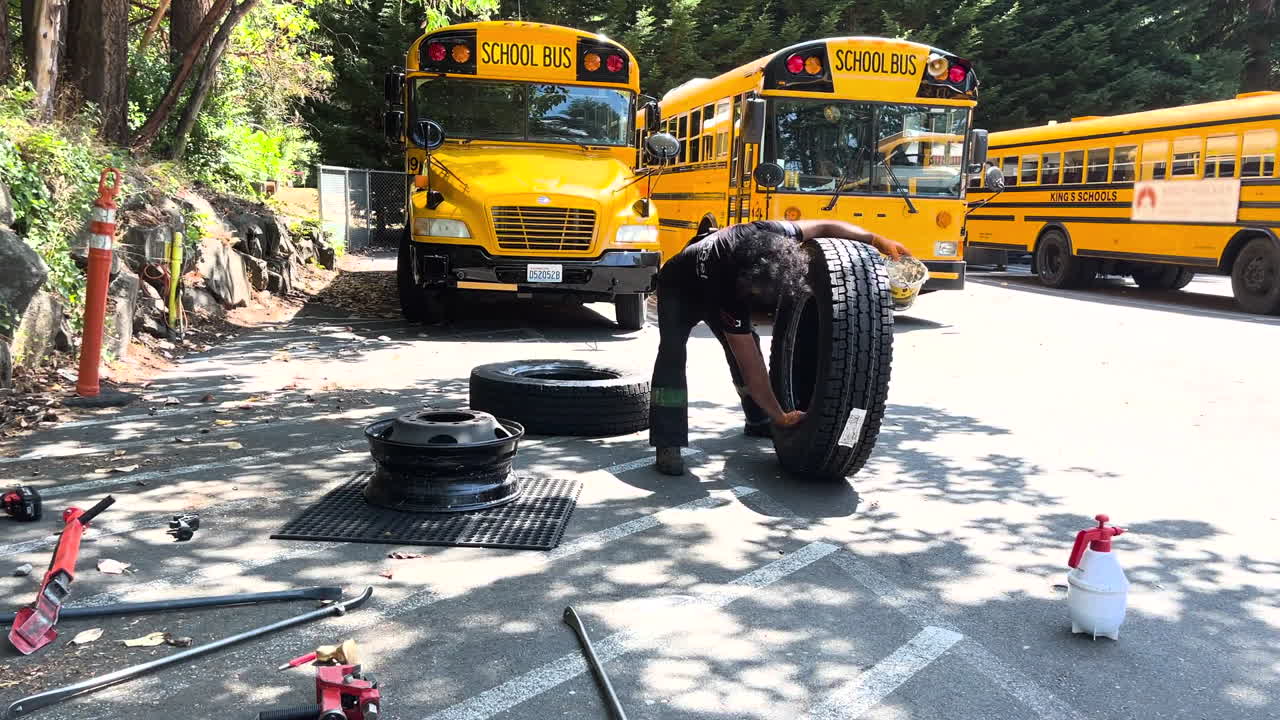 Latino man in uniform provides maintenance and tire repair service to school buses