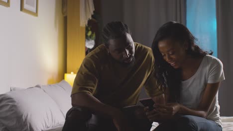 young couple relaxing at home at night in bedroom looking at mobile phone together 6