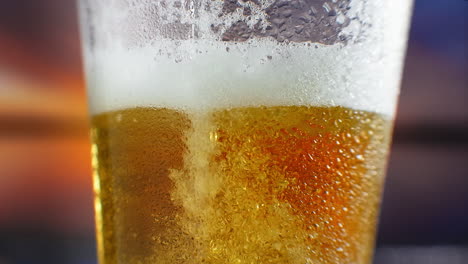 slow-motion macro cold beer is poured into a glass with perspiration. beer bubbles rise to the surface.