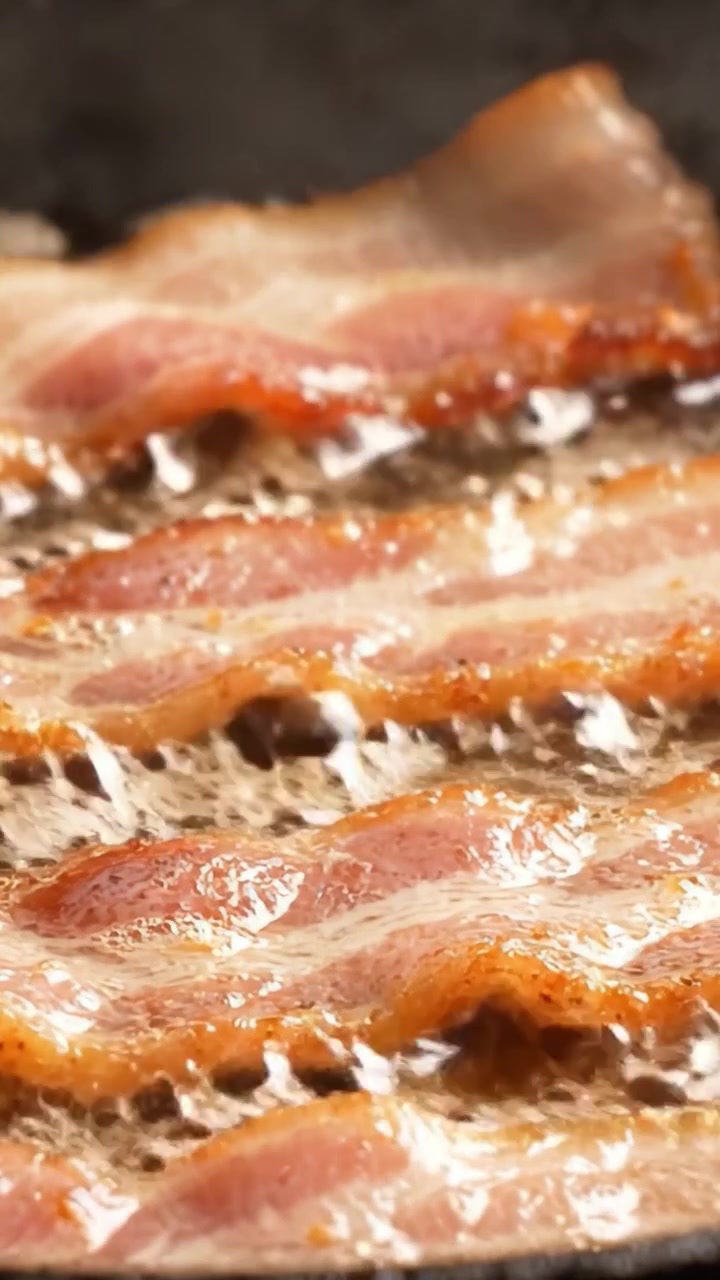 Sydende bacon steger til perfektion: Et nærbillede af sprøde strimler på en pande, der fanger den appetitlige tekstur og smagfulde safter i hvert billede.
