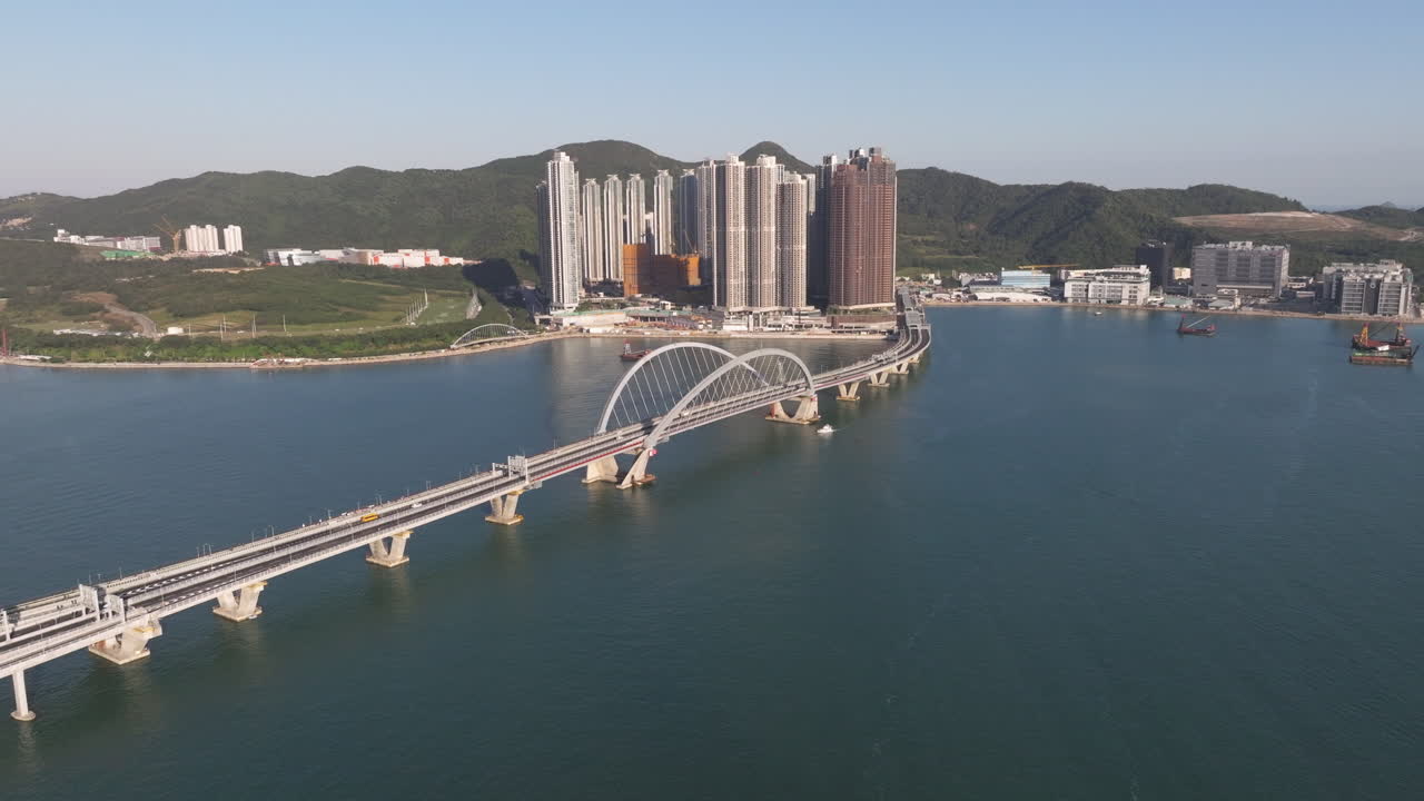 el tráfico conduce sobre el nuevo puente de enlace de la bahía cruzada con los altos edificios del parque lohas en un día soleado en el fondo