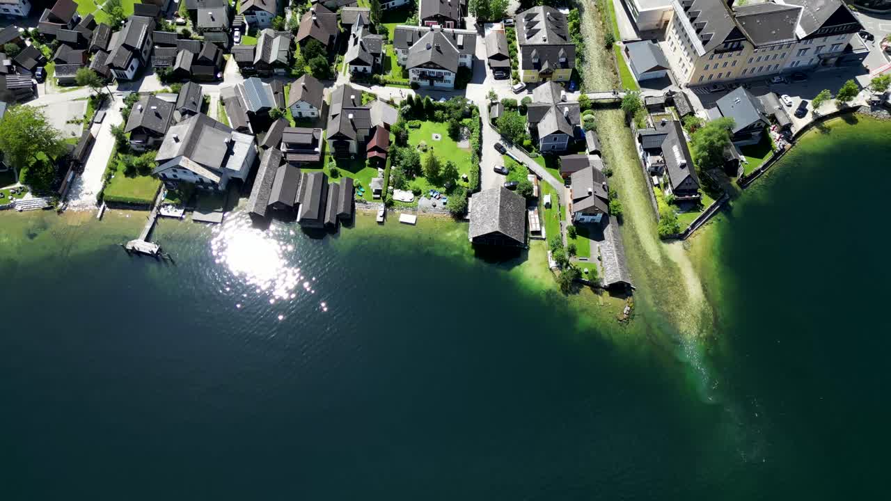 Drone footage showcases charming homes nestled along the pristine blue lake in Hallstatt, Austria, surrounded by stunning alpine landscapes and tranquil, picturesque views.