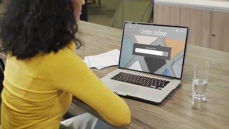 biracial woman at table using laptop, online shopping for clothes, slow motion