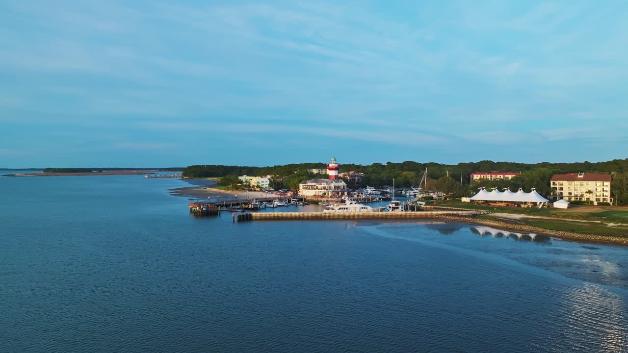 Drone approach over harbor town pier with lighthouse and boats in calm afternoon