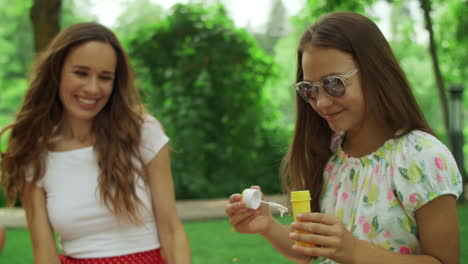 woman and girl playing with soap bubbles in park. family laughing outdoors