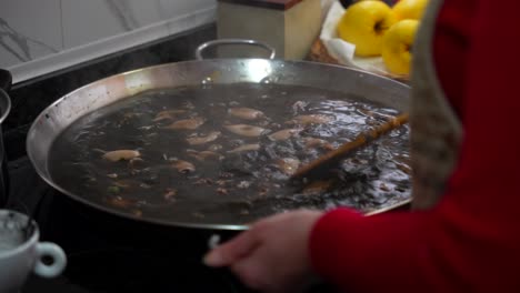 chef cocinando paella de tinta de calamar, agita agua negra humeante y agita la sartén