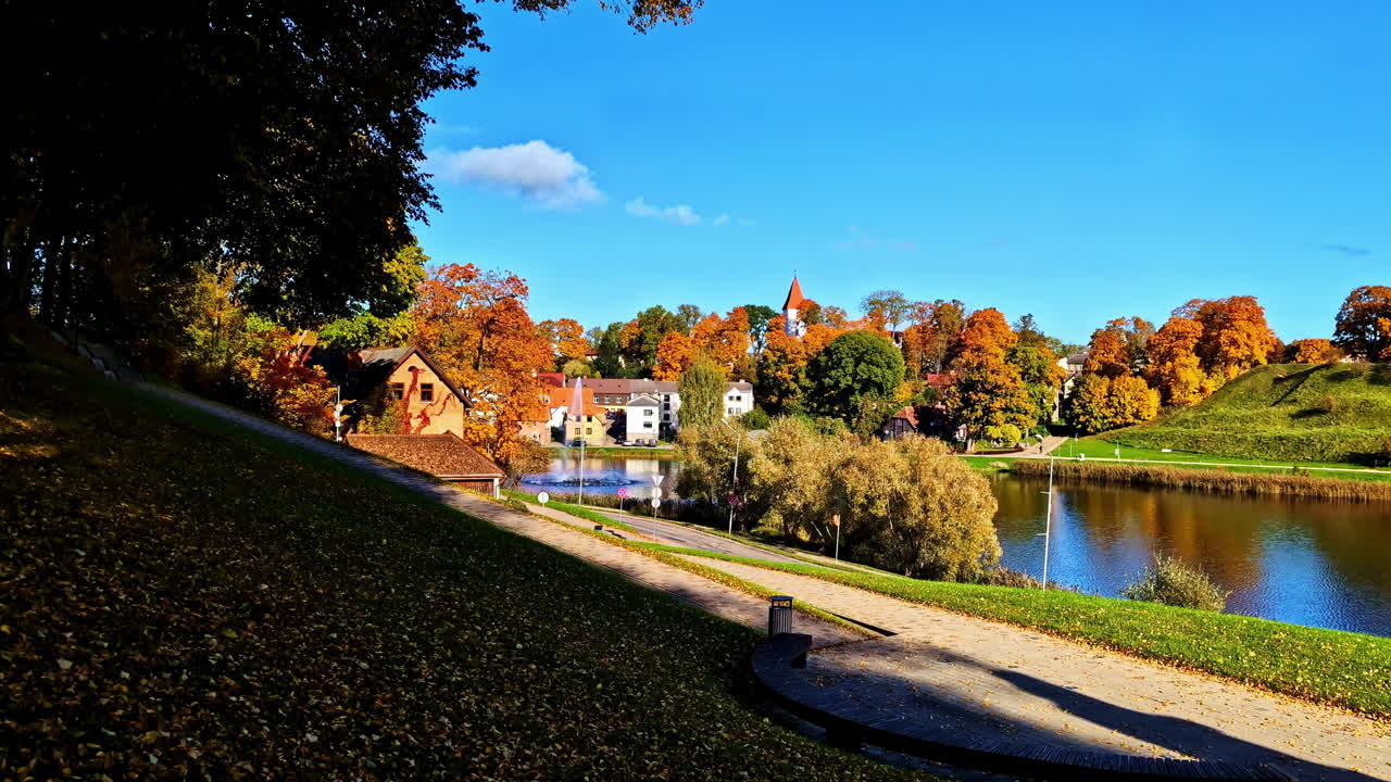 Scenic village park by a small lake, surrounded by vibrant autumn-colored trees.