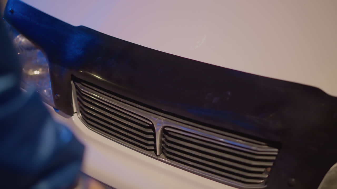 Meticulous restoration under workshop lighting, Gentle dismantling of vehicle front during quiet hours, Methodical process of removing front bumper with attention to detail at night