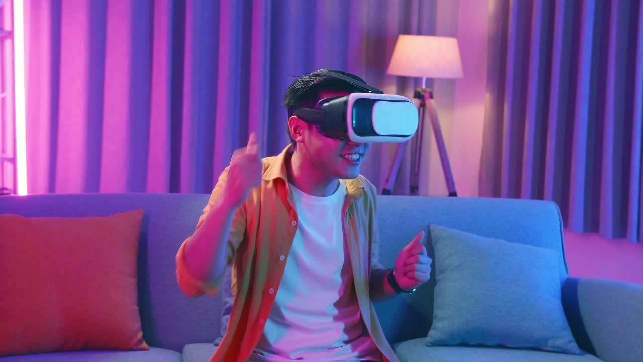 Giovane uomo asiatico che indossa un visore VR e balla in salotto, con colori ciano e magenta