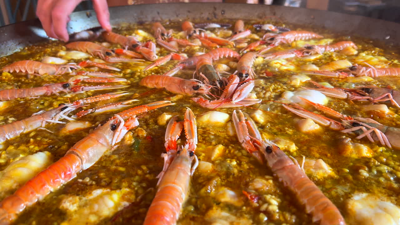 cocinando un enorme plato tradicional español de paella de mariscos con camarones, vieiras de san jacobo y cigala langostas noruegas nephrops norvegicus, arroz cocido con mariscos, marbella españa, tiro de 4k