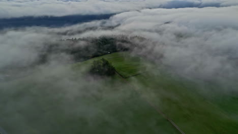 Toma-Aérea-De-Un-Paisaje-Verde-Con-Nubes-Y-Niebla-Flotando-Sobre-él.