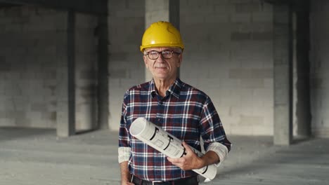 portrait of caucasian senior engineer holding plans and standing on construction site.