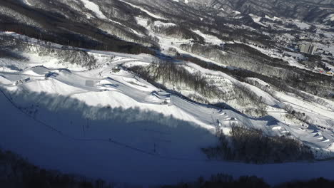 Sobrevuelo-Aéreo-Hermosa-Estación-De-Esquí-De-Yongpyong-Durante-El-Día-Soleado-Con-Nieve-Y-árboles