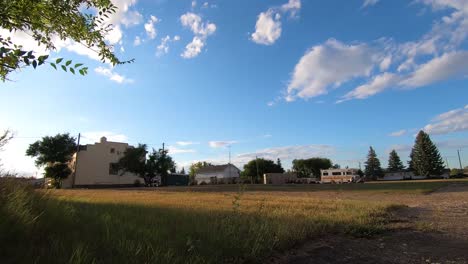 timelapse - thick clouds moving over head of a yard in a small town across from old buildings and big trees near alberta canada