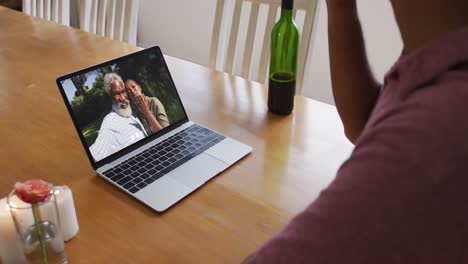 Mixed-race-man-sitting-at-table-using-laptop-making-video-call-with-friends