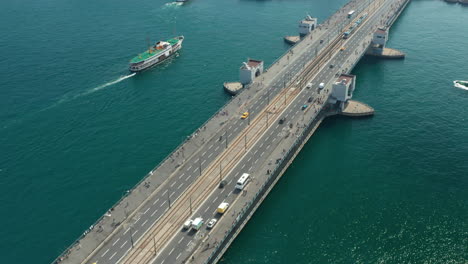 Galata-Bridge-over-Bosphorus-Water-with-Boat-and-Car-traffic-and-Seagulls-in-passing-by,-Aerial-tilt-down-Birds-Eye-View